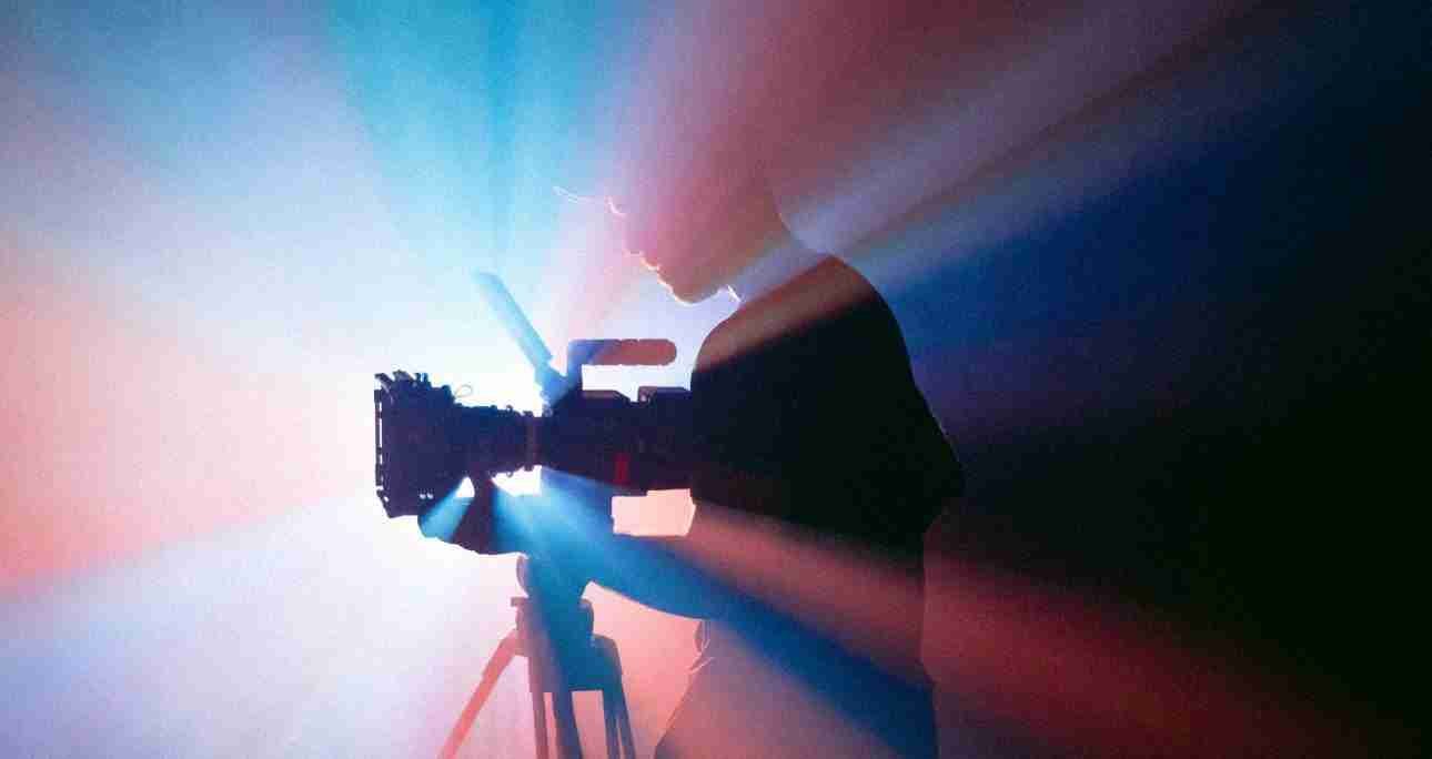 Silhouette of a videographer filming with a professional camera, illuminated by vibrant color light beams, representing video content strategies for higher engagement.