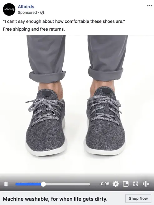 Close-up of a person wearing dark gray Allbirds sneakers with gray laces. Their pants are rolled up slightly,