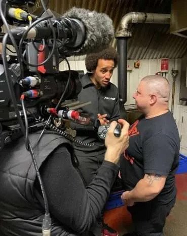 Behind the scenes photo of Omah talking with smoke house chef about cooking vegetarian food. Camera man is close to them with camera on his shoulder.